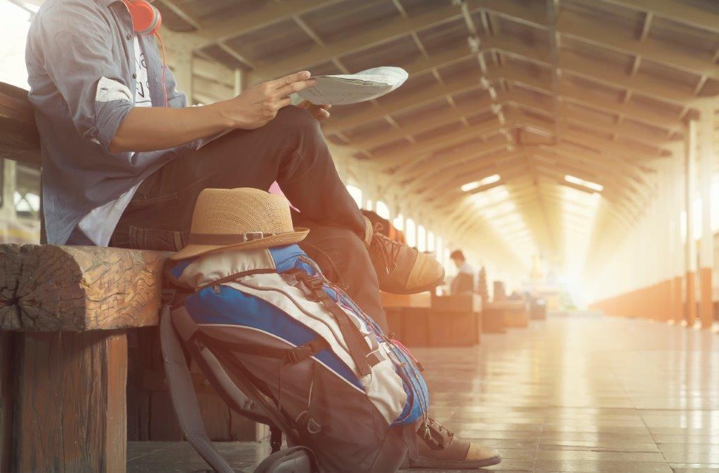 Une personne assise sur un banc attend dans une gare, son sac de voyage posé à côté
