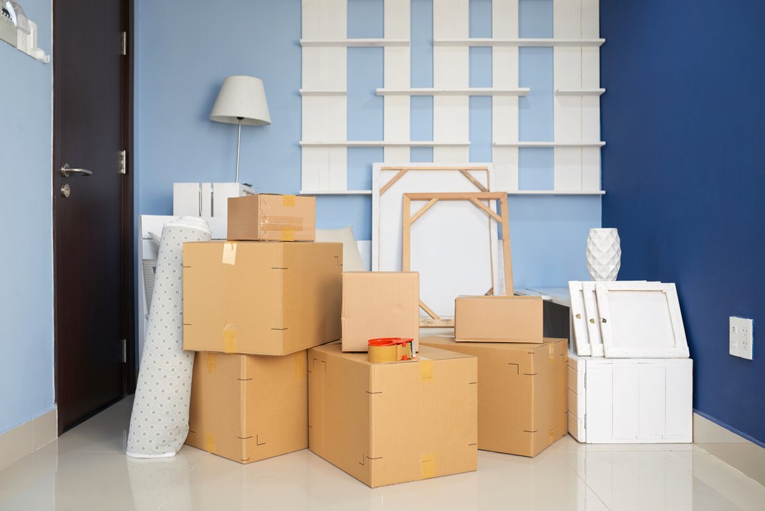 move-home-cardboard.jpg Moving boxes and decorative objects are stacked in a room with blue walls.