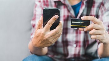 Une personne tient un téléphone dans une main et une carte bancaire dans l'autre