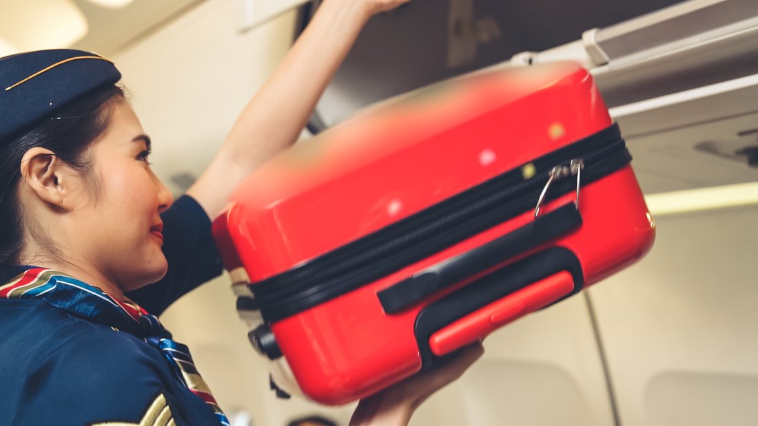 Une hôtesse de l'air range une petite valise rouge dans le compartiment au-dessus des sièges dans l'avion