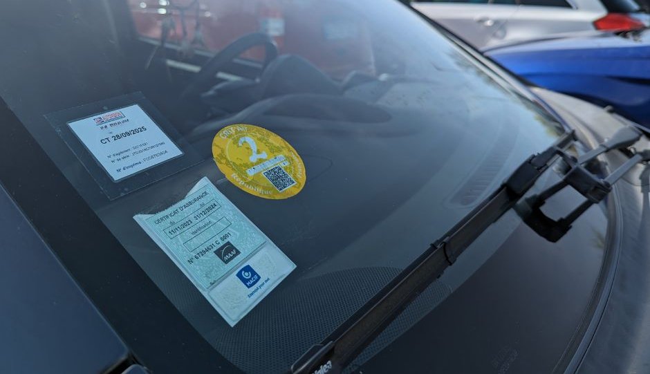 Vue rapprochée du pare-brise d'une voiture avec différentes vignettes apposées dessus