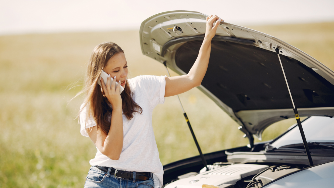 Une femme ouvre le capot de la voiture et appelle son assurance