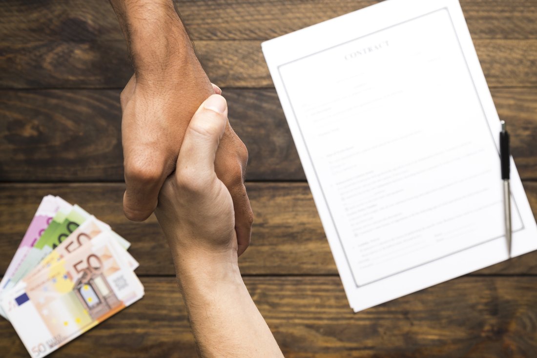 accord-mains-contrat.jpg Deux personnes se serrent la main, on peut voir en arrière plan un contrat ainsi que plusieurs billets.