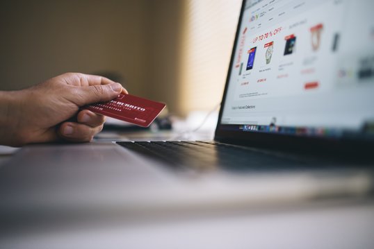 payment-credit-card-online.jpg A person is in front of his computer, on an e-commerce site, holding a credit card without in hand.