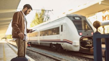 Un homme se tient sur le quai, une valise à la main, et semble attendre son train