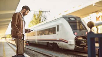 Un homme se tient sur le quai, une valise à la main, et semble attendre son train