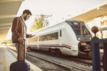 A man is standing on the platform, suitcase in hand, and appears to be waiting for his train