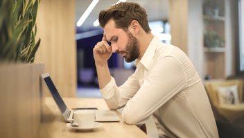 Un homme, la main sur la tempe, regarde un ordinateur portable, assis à une table
