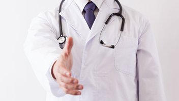 Un médecin en blouse blanche et stéthoscope autour du coup tend la main pour la serrer à quelqu'un