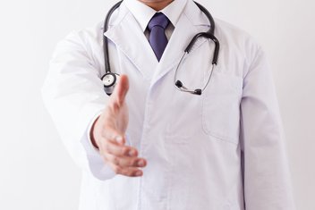 A doctor in a white coat with a stethoscope around his neck reaches out to shake someone's hand