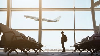 A passenger inside the airport watches a plane taking off from the window