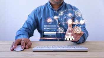 Un homme assis à une table touche un écran tactile devant une souris et un clavier