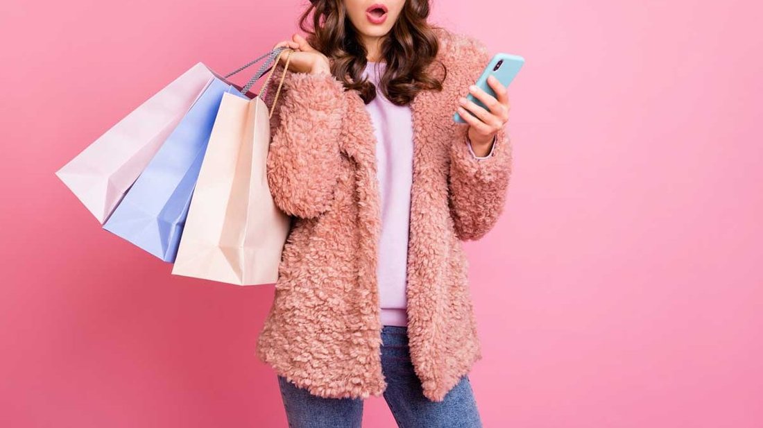 A woman holds her phone in one hand and shopping bags in the other