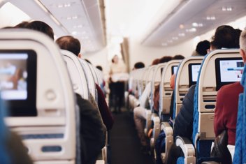 Rows of seats in an airplane, passengers are seated and seen from behind