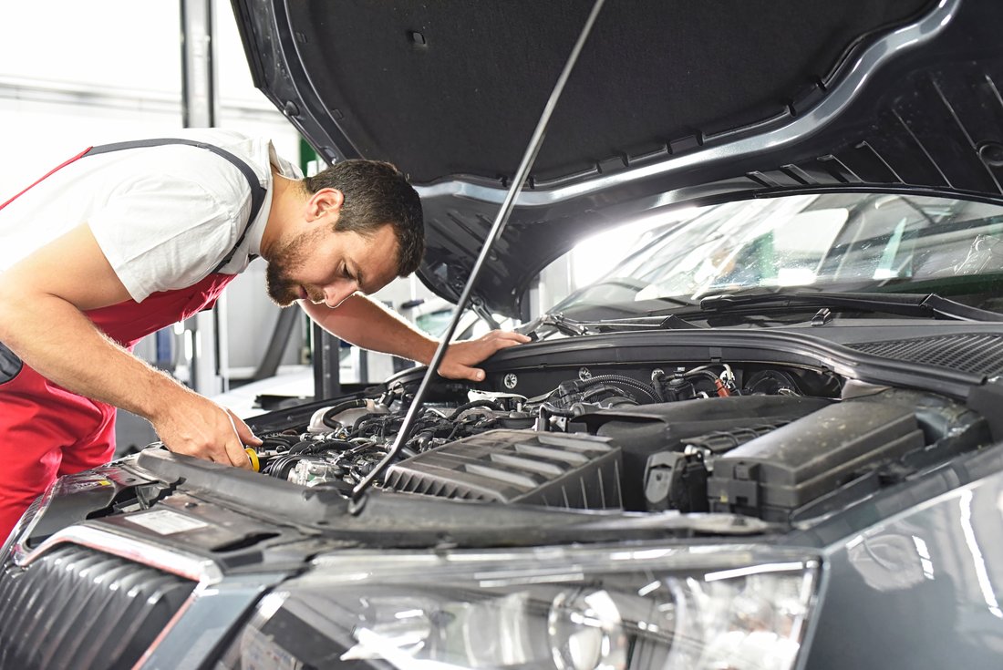 A man, bent over a bonnet, repairs a car