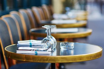 Row of tables and chairs on the terrace, with glasses, cutlery and ashtrays laid out on the tables
