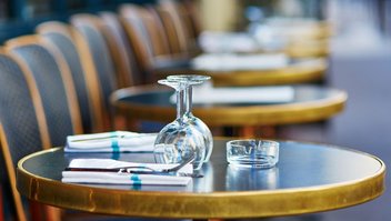 Rangé de tables et chaises en terrasse, avec verres, couverts et cendrier disposés sur la table