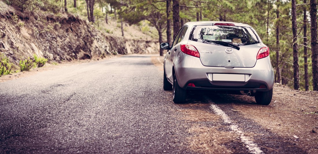 A car is parked along a road in the forest.
