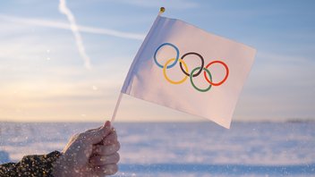 Une main agite un drapeau des Jeux olympiques sur fond de mer